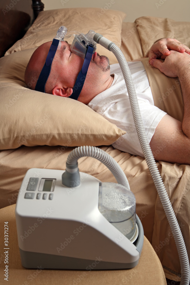 Naklejka premium Man with sleep apnea using a CPAP machine in bed.