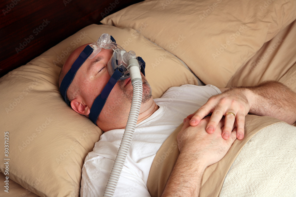 Man with sleep apnea using a CPAP machine in bed. Stock-foto | Adobe Stock