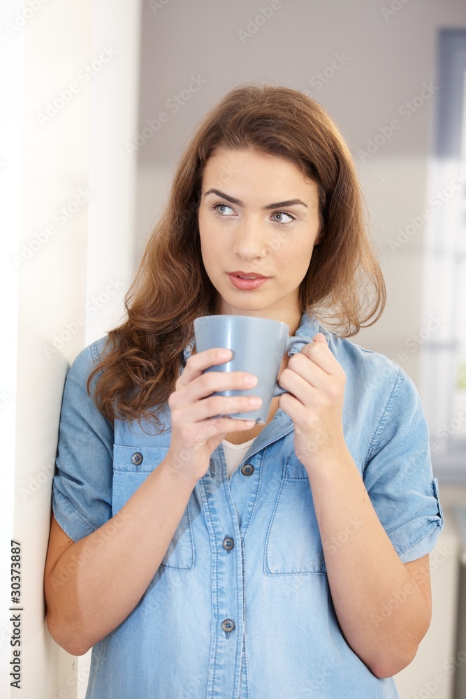 Young woman drinking tea at home standing