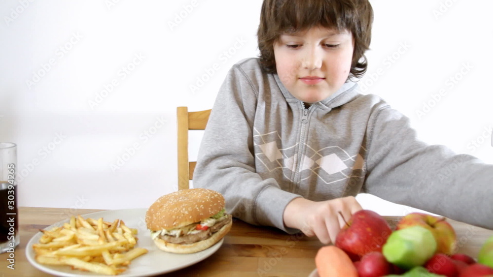 Young boy choosing fast food instead of vegetables and fruits Young boy choosing fast food instead of vegetables and fruits