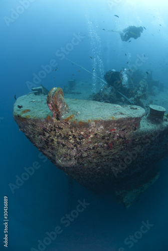 Silhouettes of scuba divers exploring the bow of a shipwreck.