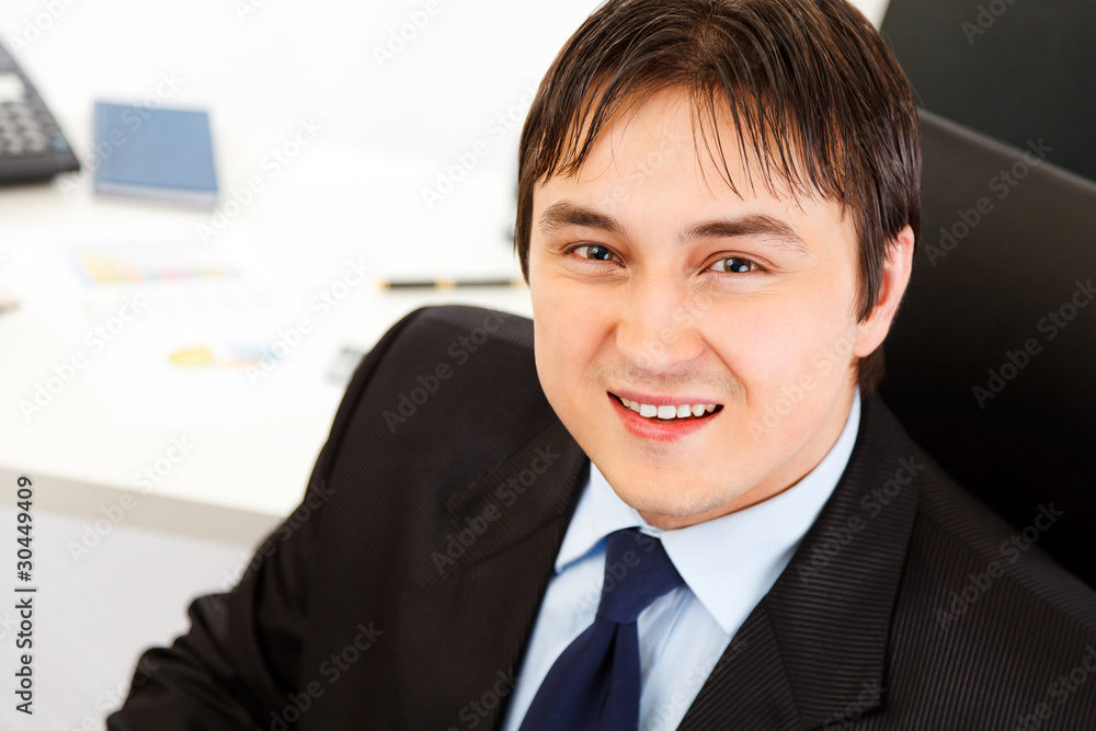 Pleased modern business man sitting at office desk. Pleased modern business man sitting at office desk.