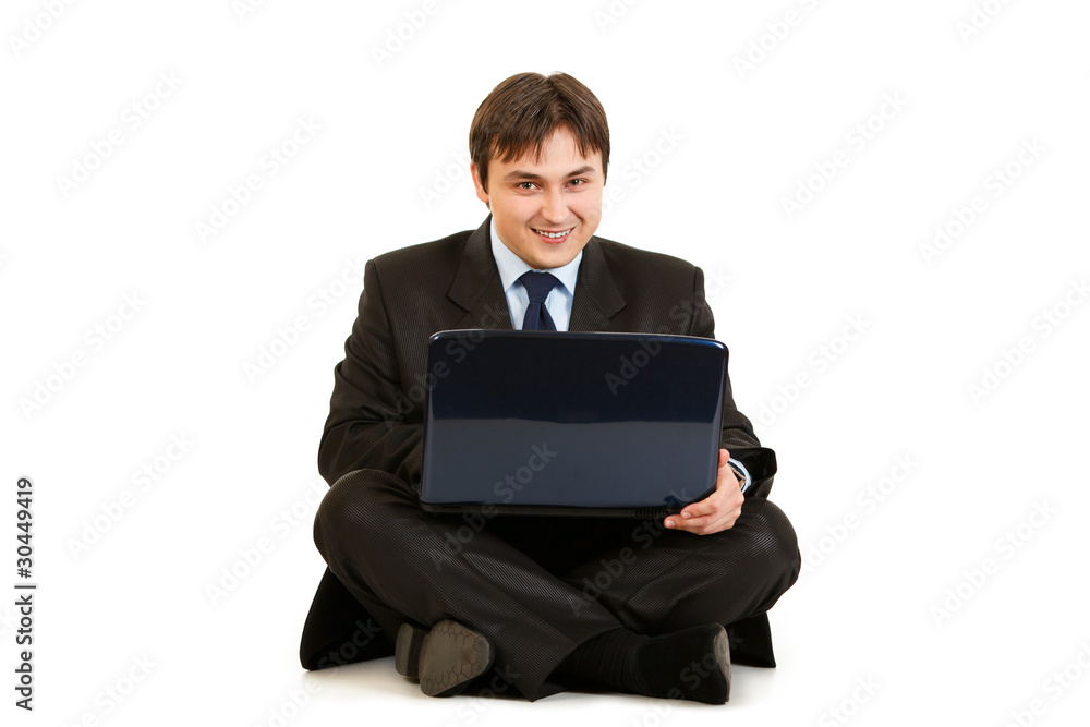 Smiling businessman sitting on floor and working on laptop Smiling businessman sitting on floor and working on laptop