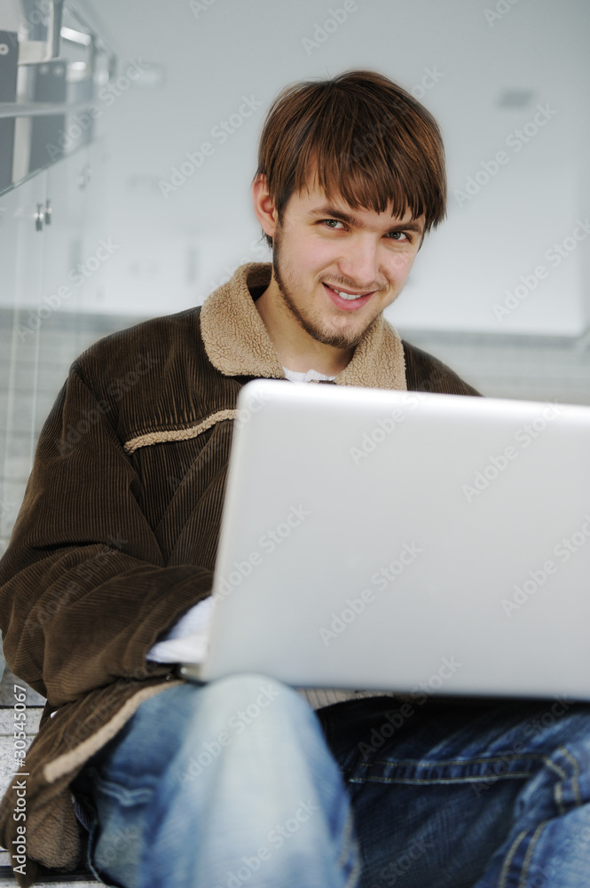 Relaxed young man working on laptop while sittinig on steps Relaxed young man working on laptop while sittinig on steps