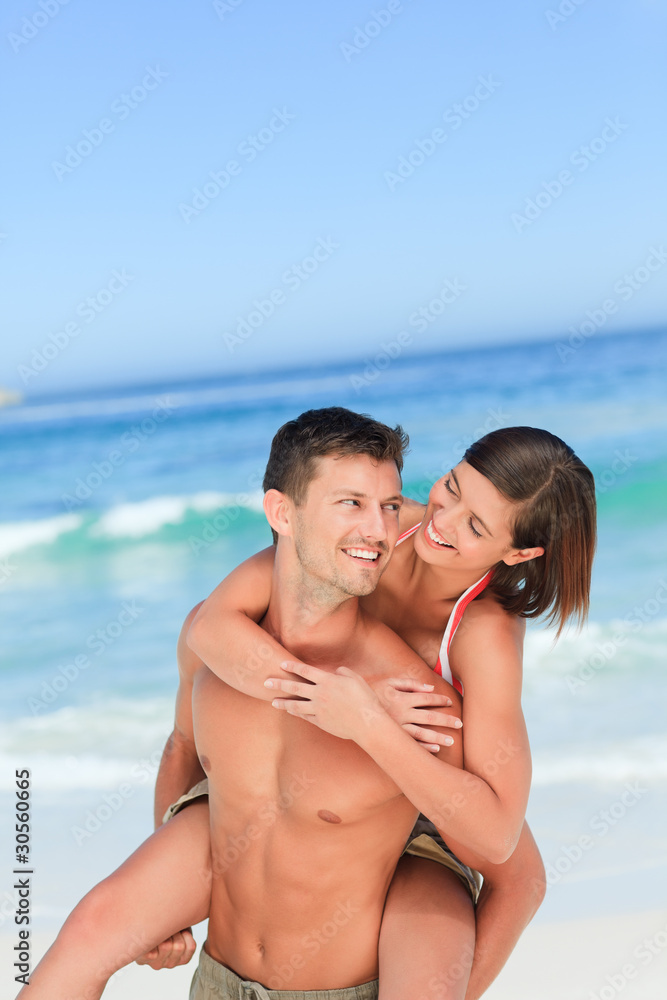 Handsome man having wife a piggyback on the beach Handsome man having wife a piggyback on the beach