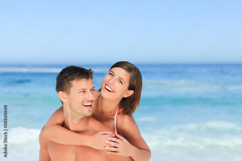 Handsome man having wife a piggyback on the beach Handsome man having wife a piggyback on the beach