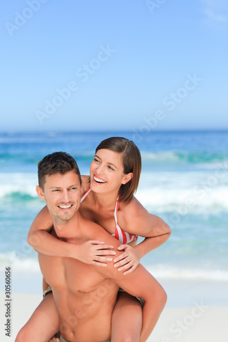 Handsome man having wife a piggyback on the beach