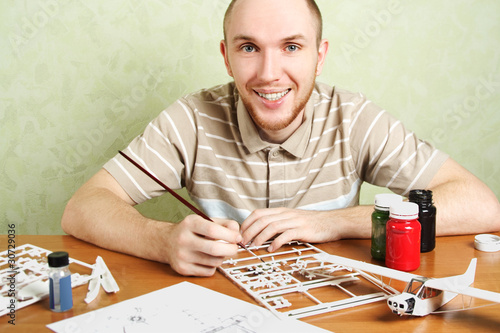 man assembling plastic airplane model and painting pieces, smili photo