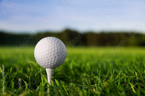 Golf ball on tee. Green field, blue sky.