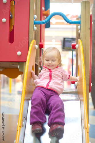 Young adorable baby sliding down slide on playground in mall
