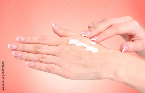 Closeup of beautiful female hands applying hand cream  on red ba