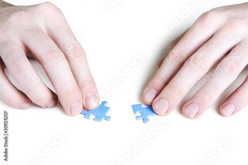 closeup of mans hands assembling two blue puzzle pieces, isolate