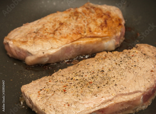 Two Strip Steaks Sizzling in a Skillet