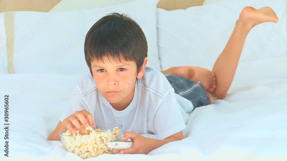 A little boy eating popcorn in front of the tv A little boy eating popcorn in front of the tv