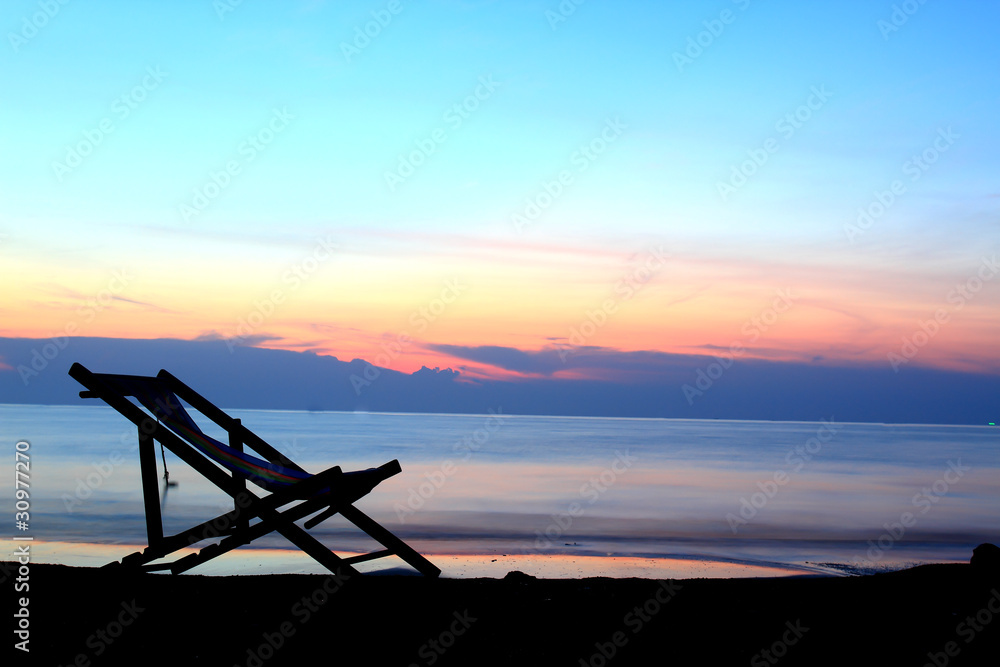 one deckchairs on beach at sunset .