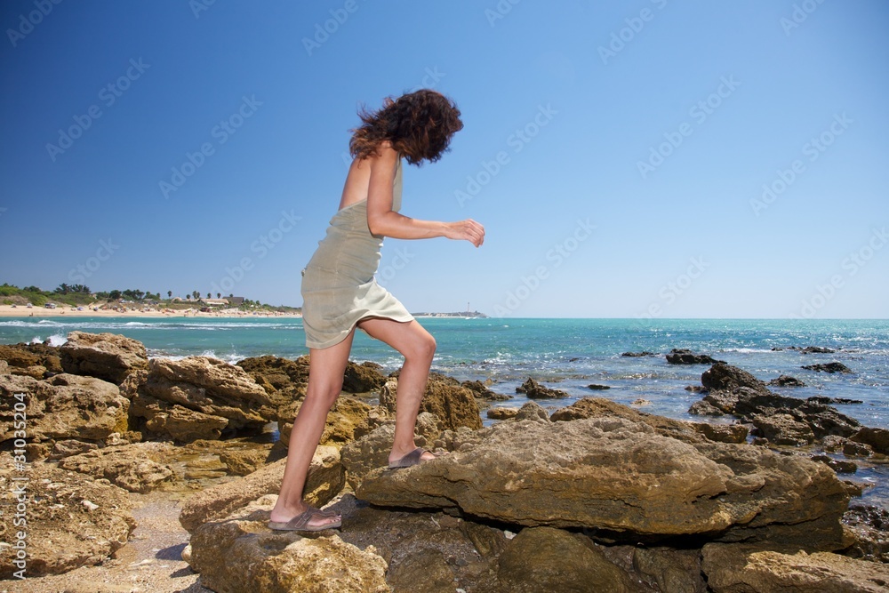 woman walking on rocks next ocean