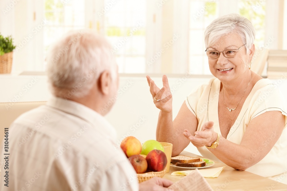 Elderly wife chatting to husband at breakfast Elderly wife chatting to husband at breakfast