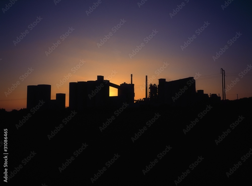 Concrete Factory Silhouette, Backlit By The Sun On The Horizon