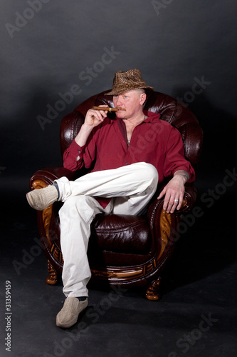 Senior man sitting in large leather armchair and smoking cigar photo