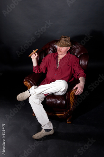 Senior man sitting in large leather armchair and smoking cigar