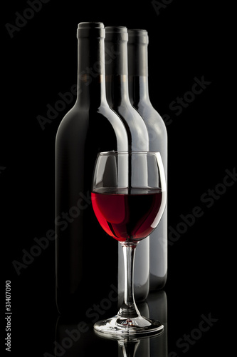 Elegant red wine glass and a wine bottles in black background