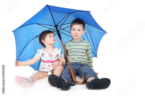 brother and the sister sit under a blue umbrella