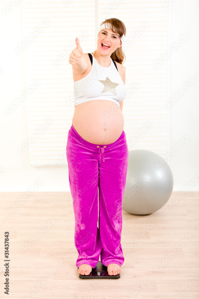 Pregnant woman standing on weight scale and showing thumbs up. Pregnant woman standing on weight scale and showing thumbs up.