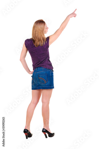 Beautiful young woman in dress pointing at wall. Rear view.
