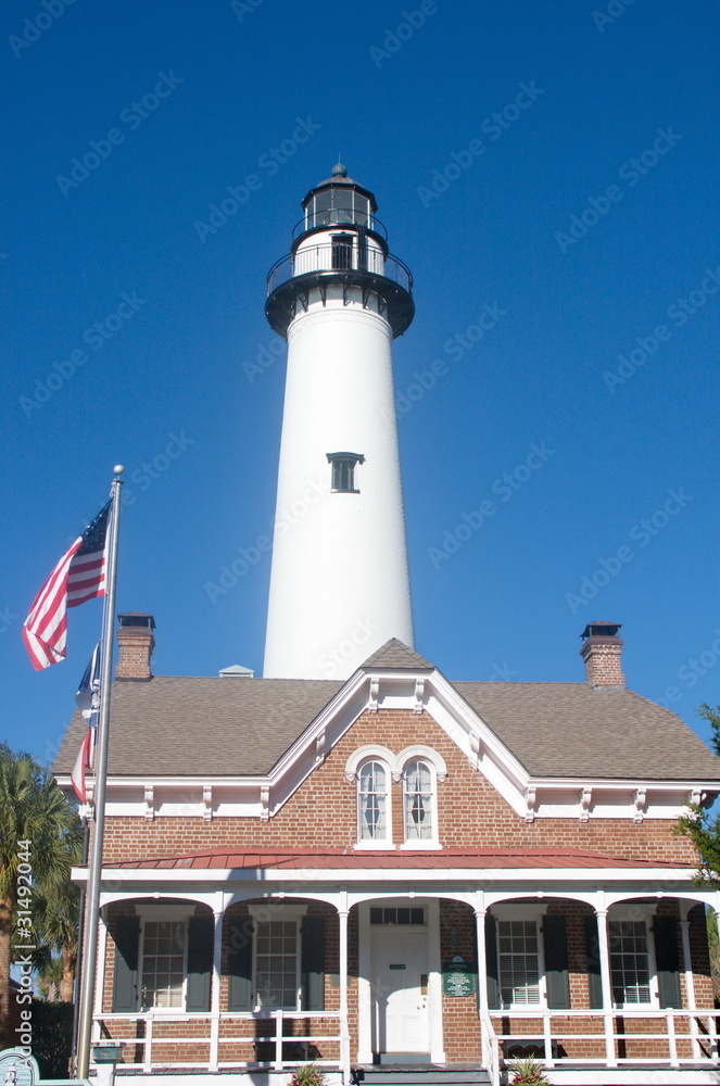 White Lighthouse Behind Brick House with American Flag White Lighthouse Behind Brick House with American Flag