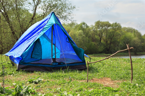 Blue tent stands on river bank in green forest on summer