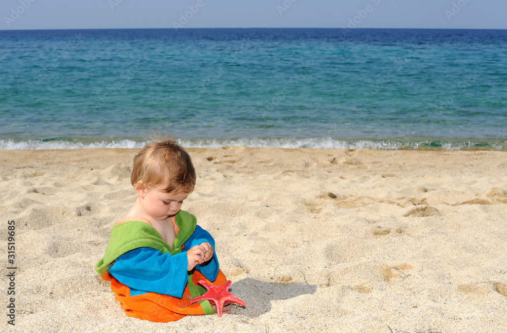 Baby girl playing with red sea stars on the beach Baby girl playing with red sea stars on the beach