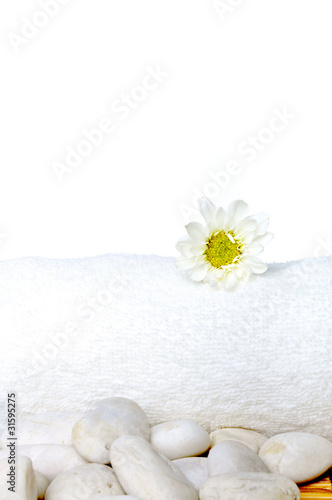 Beautiful flower on white towel and stones on the bamboo mat.