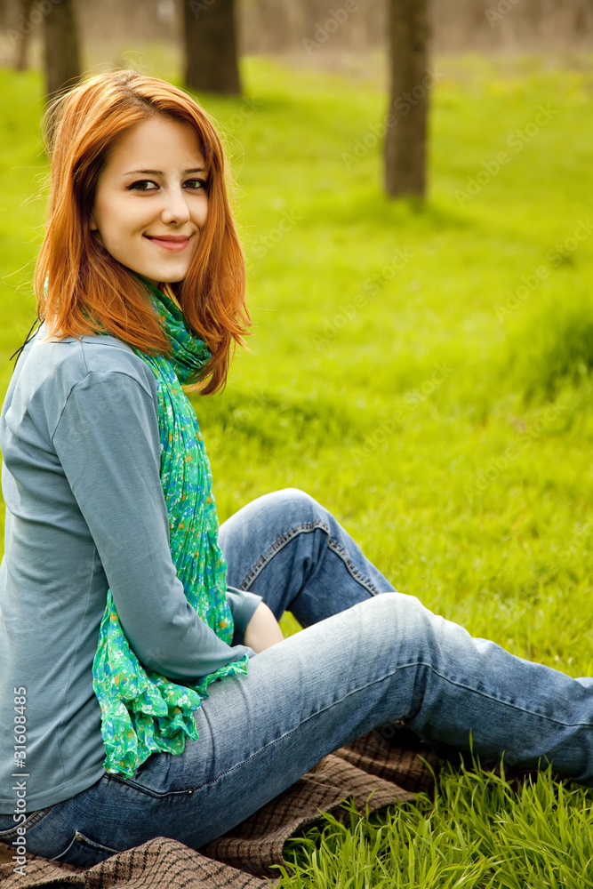 Beautiful red-haired girl sitting at green grass at park. Beautiful red-haired girl sitting at green grass at park.