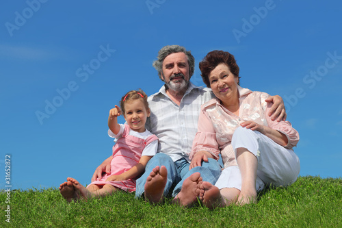 old man and woman sitting on lawn with their granddaughter