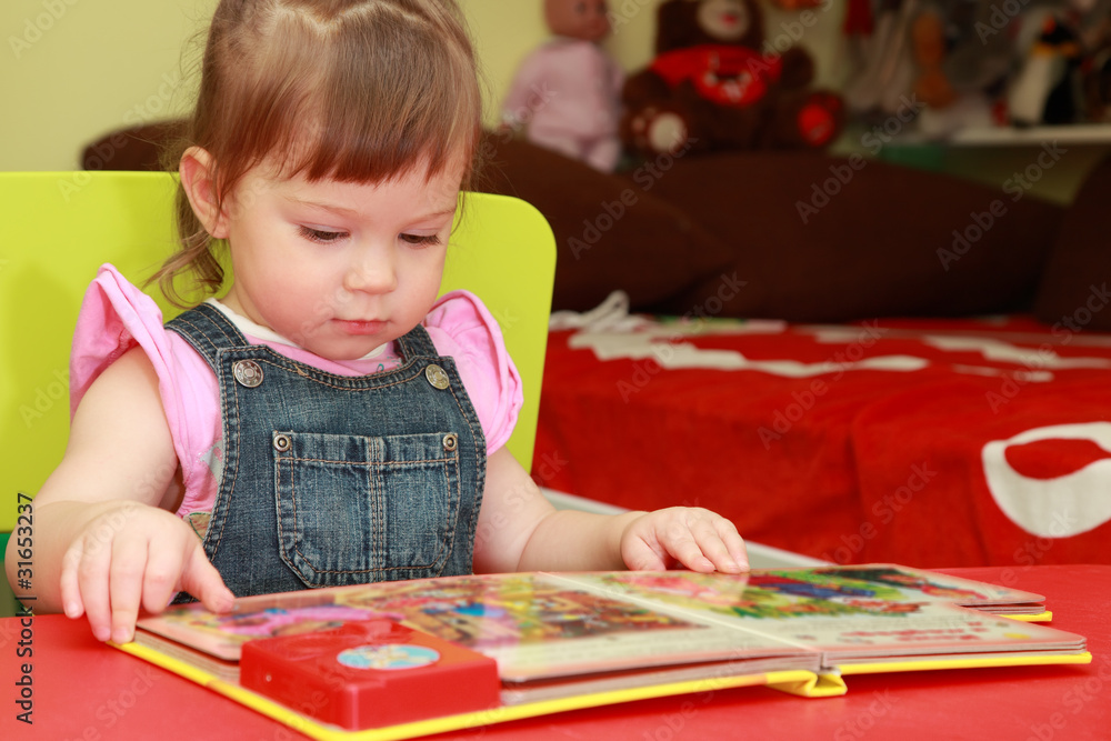 little girl in denim jumpsuit seats at table and read little girl in denim jumpsuit seats at table and read