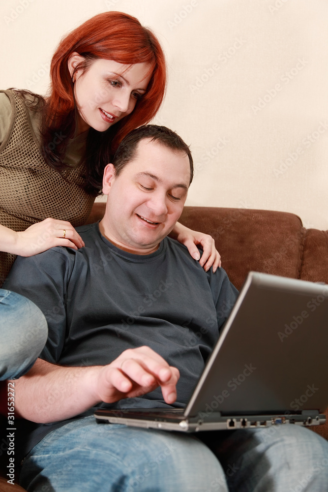 wife and husband sit on brown sofa and looking at laptop