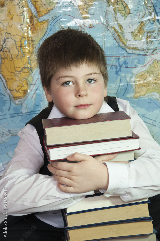 Schoolboy with a stack of books on a background map of the world Schoolboy with a stack of books on a background map of the world