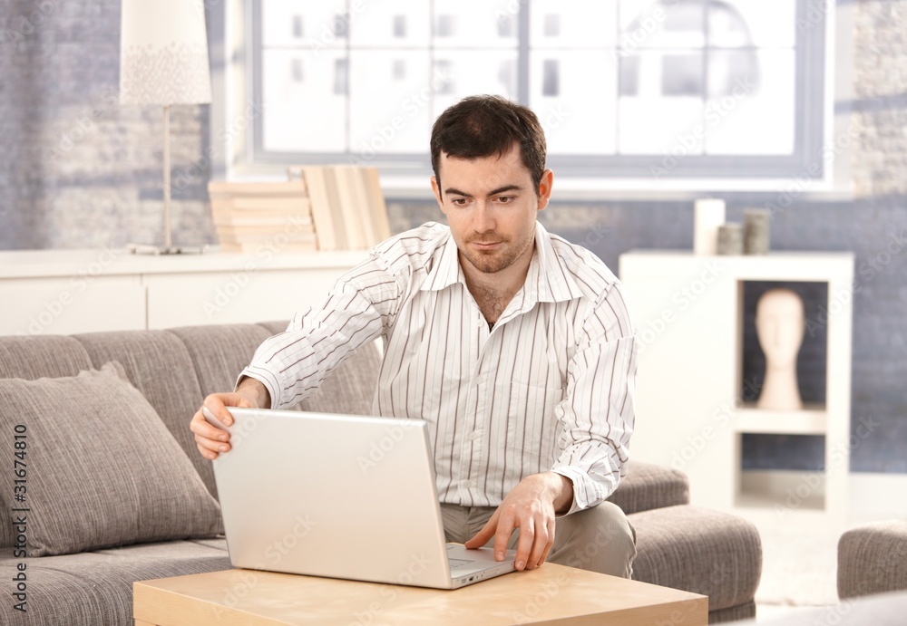 Young man using laptop at home sitting on sofa Young man using laptop at home sitting on sofa