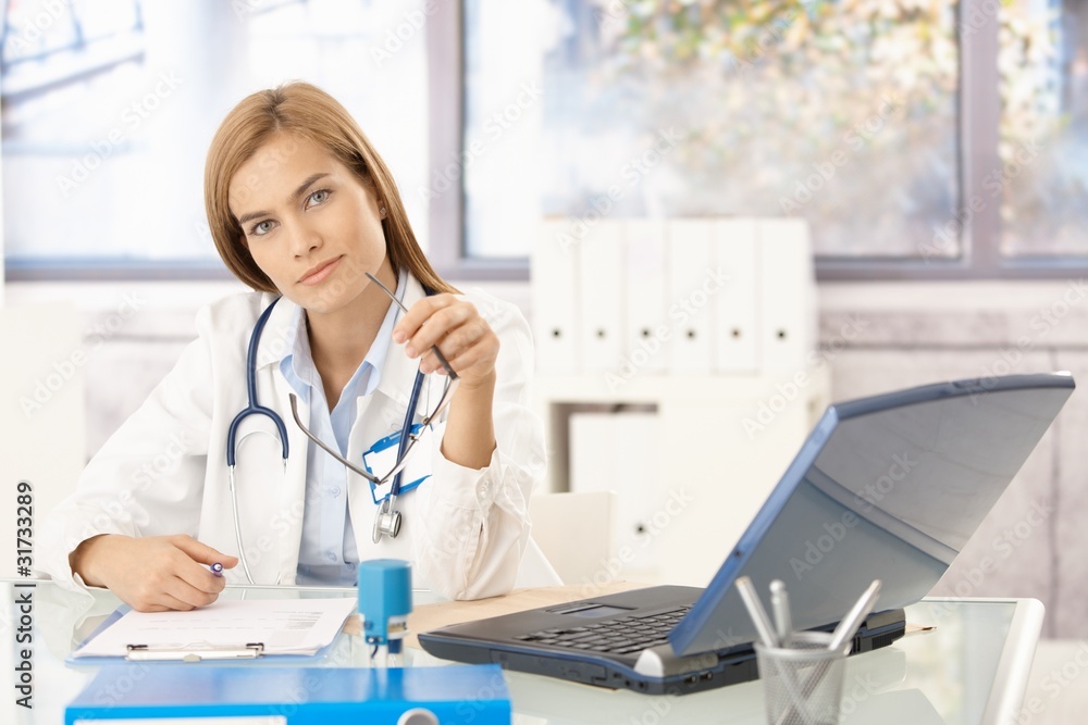 Attractive doctor writing report sitting at desk Attractive doctor writing report sitting at desk