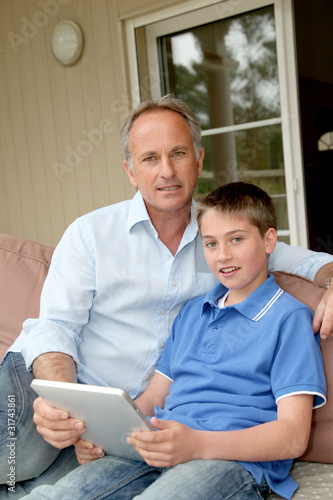Father and son sitting in sofa with electronic tablet