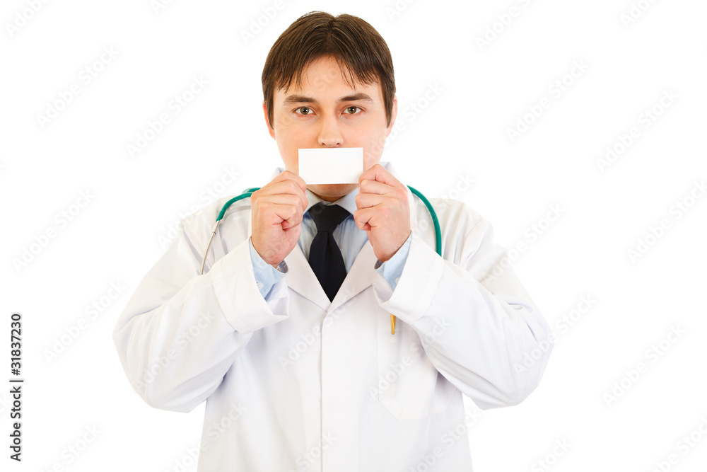 Medical doctor holding blank business card in front of mouth Medical doctor holding blank business card in front of mouth