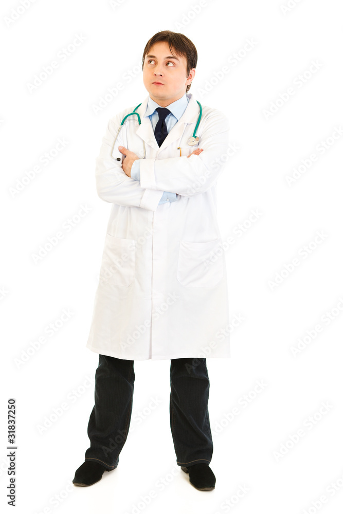 Thoughtful doctor with crossed arms looking up at copy space Thoughtful doctor with crossed arms looking up at copy space