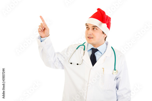 Doctor in hat of Santa Claus pointing in corner at copy space