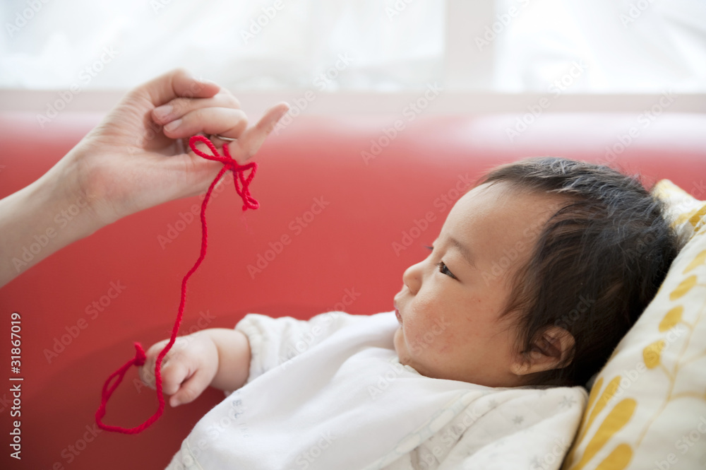 小指に結ばれた赤い糸を見つめる赤ちゃん Stock Photo Adobe Stock