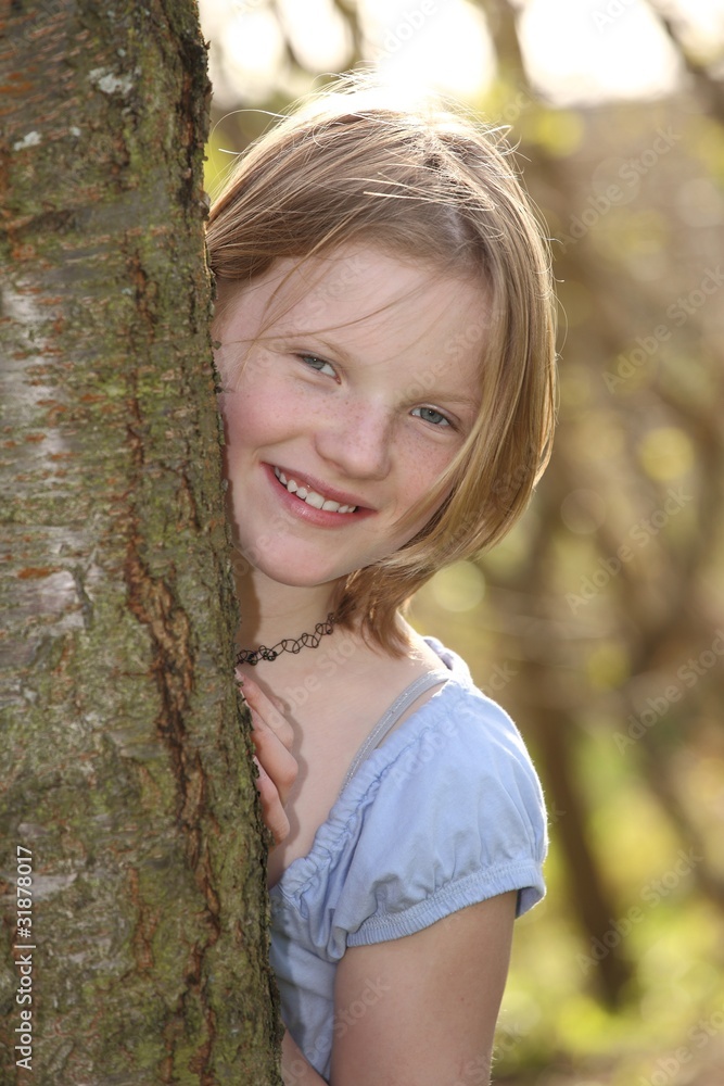 Teenager Mädchen schaut hinter einem Baum hervor Teenager Mädchen schaut hinter einem Baum hervor