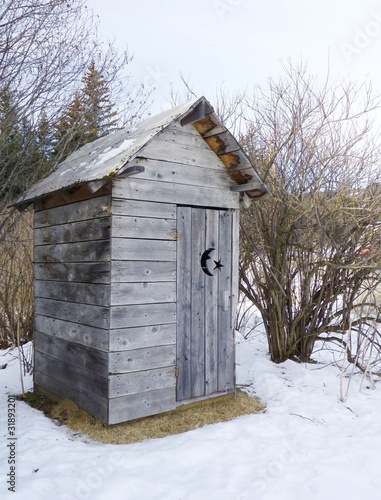 A rustic wooden outhouse in rural Alaska in winter