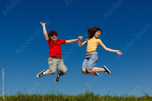 Girl and boy jumping, running against blue sky