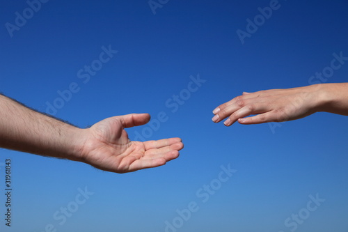 Zwei Personen reichen sich die Hände vor blauem Himmel
