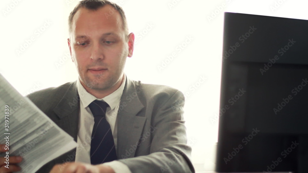 Young businessman working on computer and looking into documents Young businessman working on computer and looking into documents