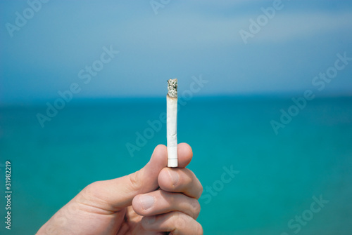 hand holds a cigarette in the background of the sea